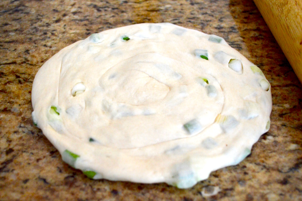 Once the dough rested, it was a matter of rolling it out into a rectangle and sprinkling it generously with chopped scallions. Then it was rolled up into a tight log before taking that log and rolling it into a spiral. It looked like a cute little snail shell! Then I rolled out that snail shell into a flat pancake.