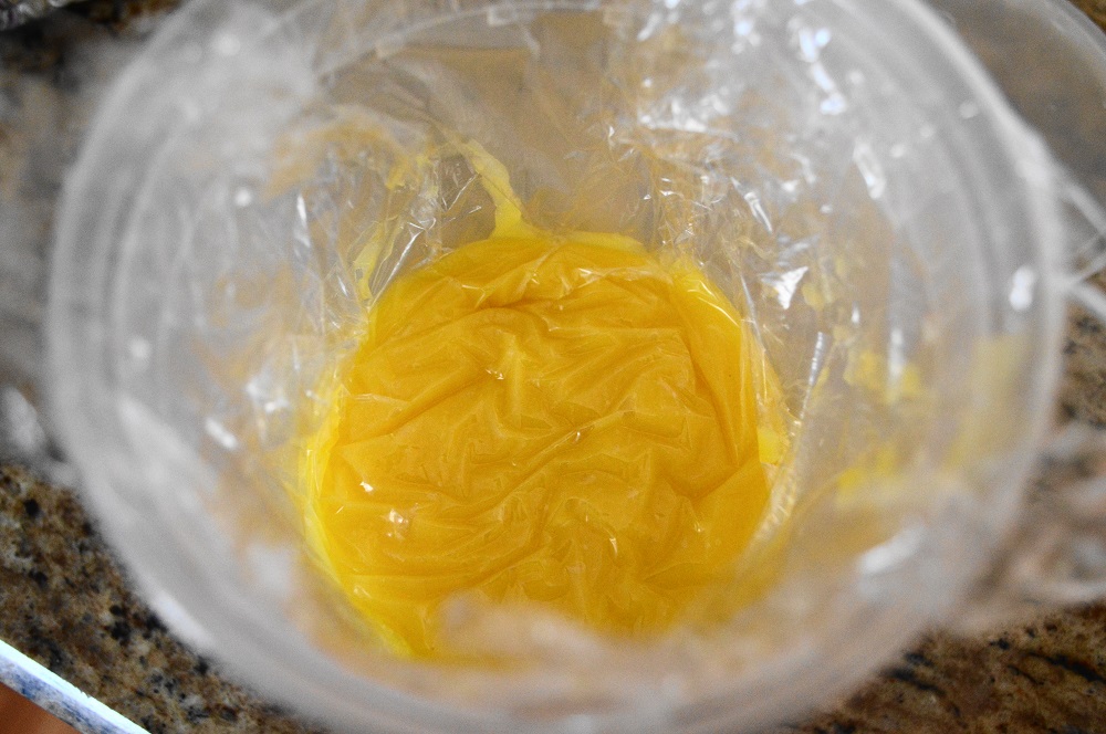 Once it had cooled just a bit, I transferred the homemade lemon curd to a container. Then I directly covered it was plastic wrap before sealing it with the lid. Putting plastic wrap directly on the lemon curd prevented a skin from forming while it chilled. 