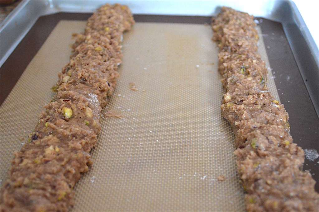 The thing about this hazelnut pistachio biscotti dough was that it was really sticky. So I made sure to have my surfaces and hands floured when I worked with it. I divided it in half and formed each half into logs that went almost the length of my sheet pan. Then I lightly pressed down on the logs to make the side on the tray flat. That formed the signature biscotti half moon shape before they baked!