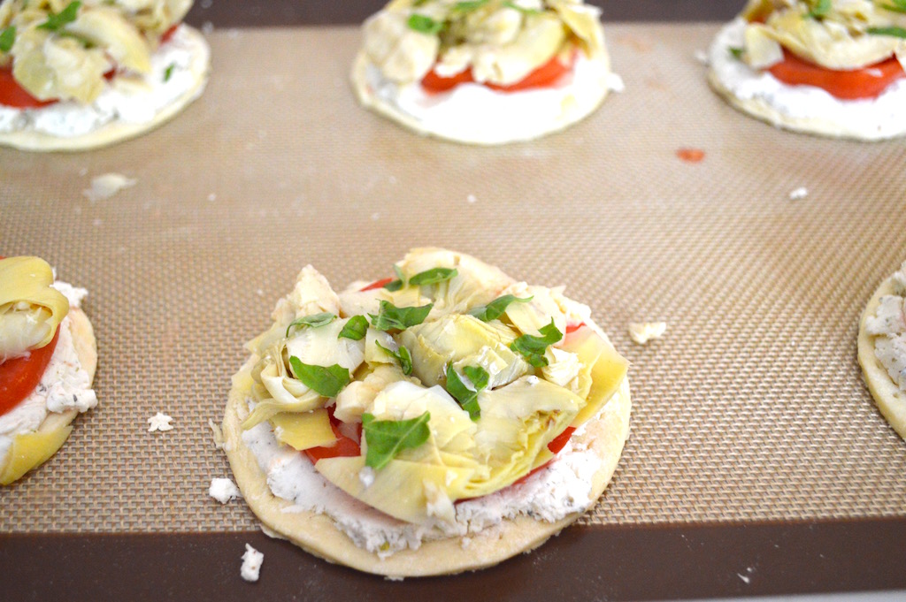 From there, forming the artichoke, tomato and goat cheese tartlets was easy! I spread an ounce of herbed goat cheese within the border of each crust. Then I layered a slice of tomato and lots of chopped artichoke on the goat cheese. To finish them up, I sprinkled chopped fresh basil on top for some herbalicious freshness!