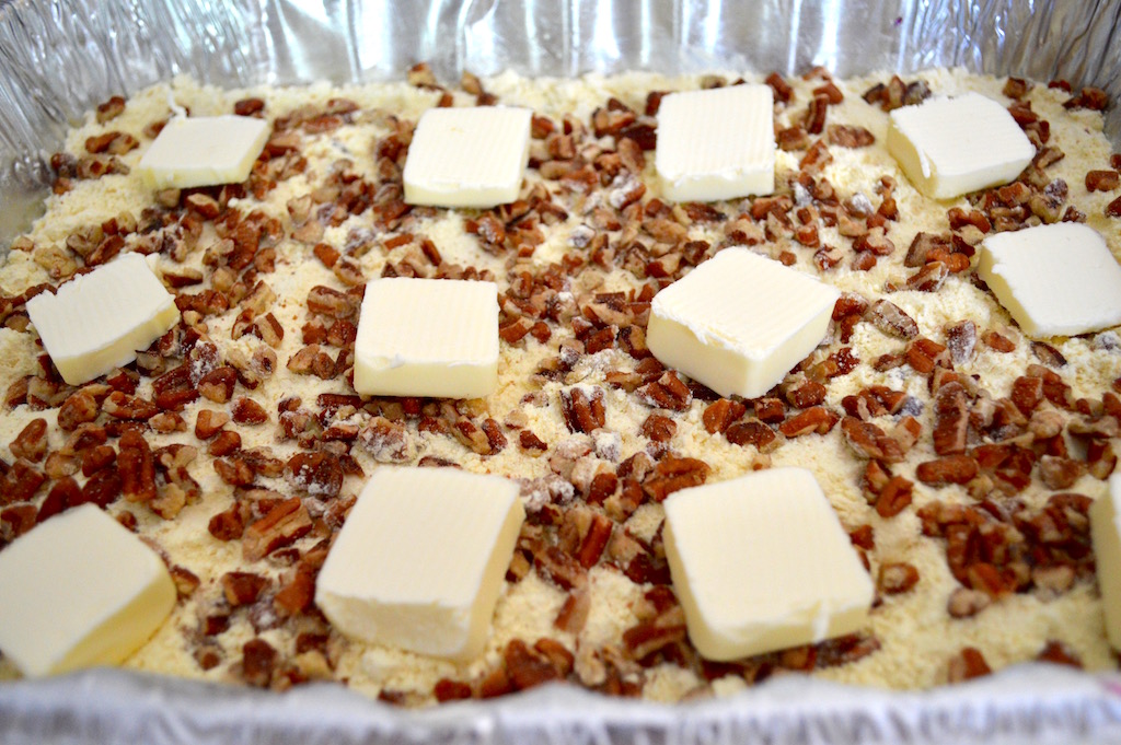 The cake portion of the pineapple blueberry dump cake was simply a box of yellow cake mix. I spread it out evenly on top of the fruit. Then I sprinkled chopped pecans on top for some crunch. The last touch was to distribute butter on the very top to make the dessert luscious. 