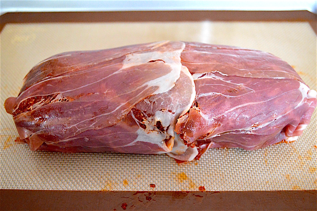 To assemble the prosciutto wrapped Italian meatloaf, I got out a sheet tray and lined it. Then I laid out the prosciutto in a single layer with the long ends hanging over the width of the pan. I slathered the sun-dried tomato pesto underneath and all around the meatloaf, then rolled it up in the prosciutto like a burrito!